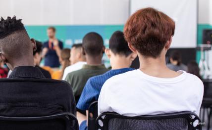 trois élèves de dos qui écoutent un professeur